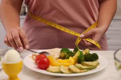 Photo of Overweight woman measuring waist while having meal at home, closeup 