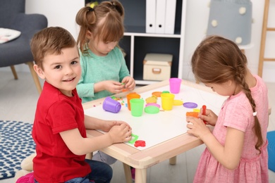 Cute little children using play dough at table indoors