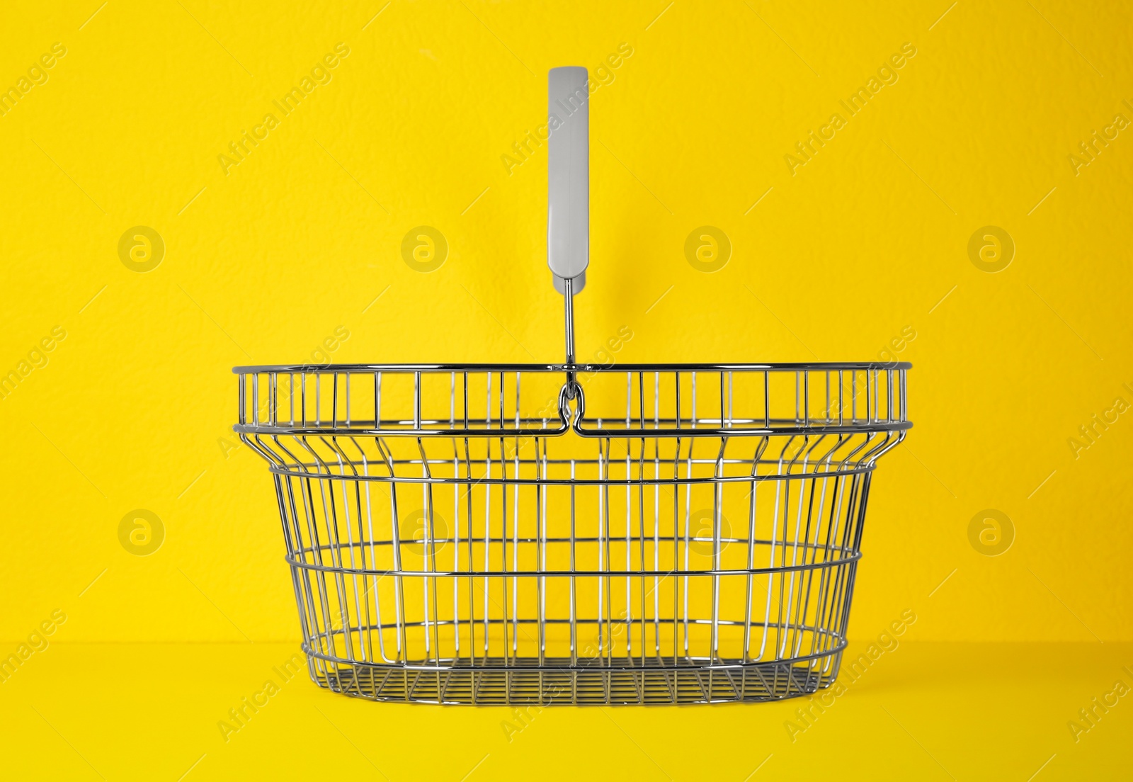 Photo of Empty metal shopping basket on yellow background