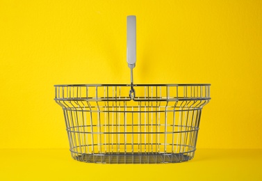 Photo of Empty metal shopping basket on yellow background