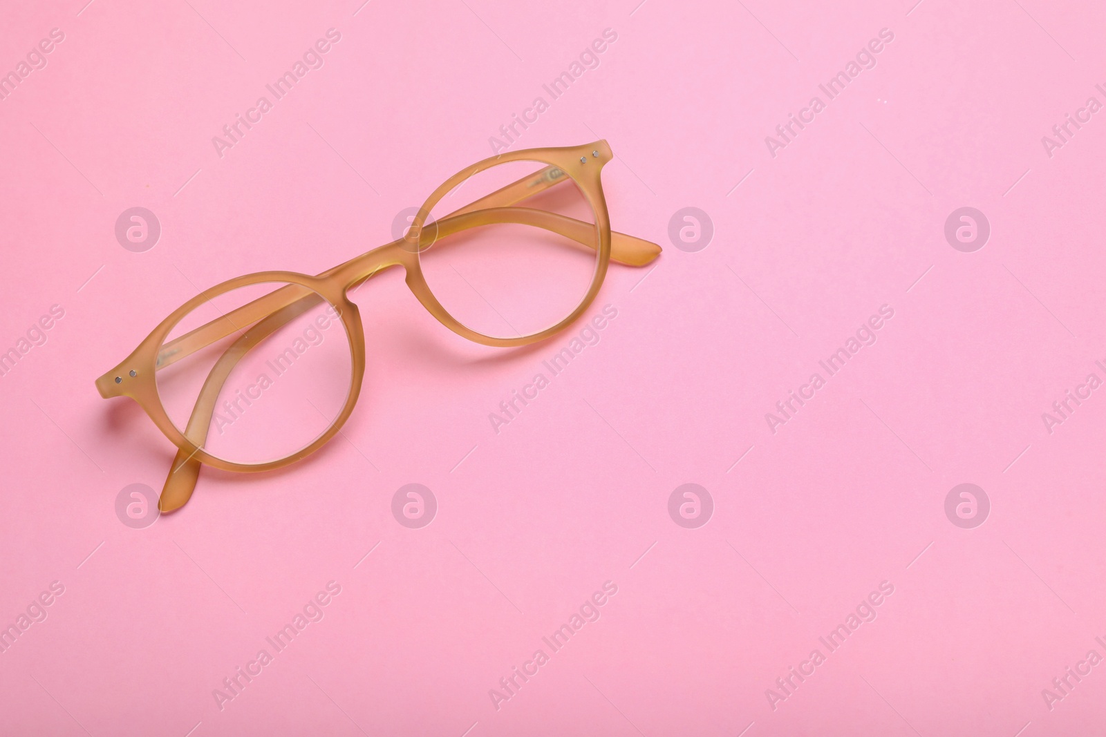 Photo of Glasses with corrective lenses on pink background, top view. Space for text