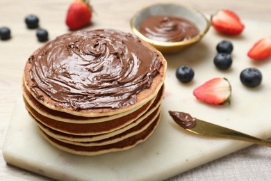 Photo of Delicious pancakes with chocolate paste, berries and knife on table, closeup. Space for text