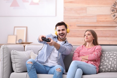 Photo of Displeased woman sitting near her man playing video games at home