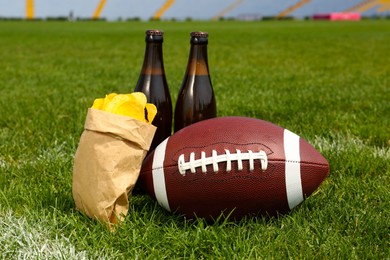 Photo of American football ball with beer and chips on green field grass in stadium