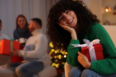 Photo of Christmas celebration in circle of friends. Happy young woman with gift box at home, selective focus