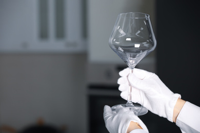 Person in white gloves checking cleanliness of glass indoors, closeup. Space for text