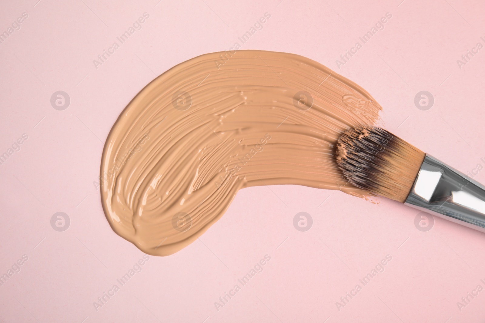 Photo of Liquid foundation and makeup brush on pink background, top view