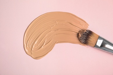 Liquid foundation and makeup brush on pink background, top view