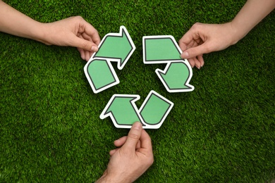 Photo of People holding paper recycling symbol above green grass, top view