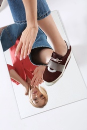 Woman in stylish shoes standing on mirror, white background