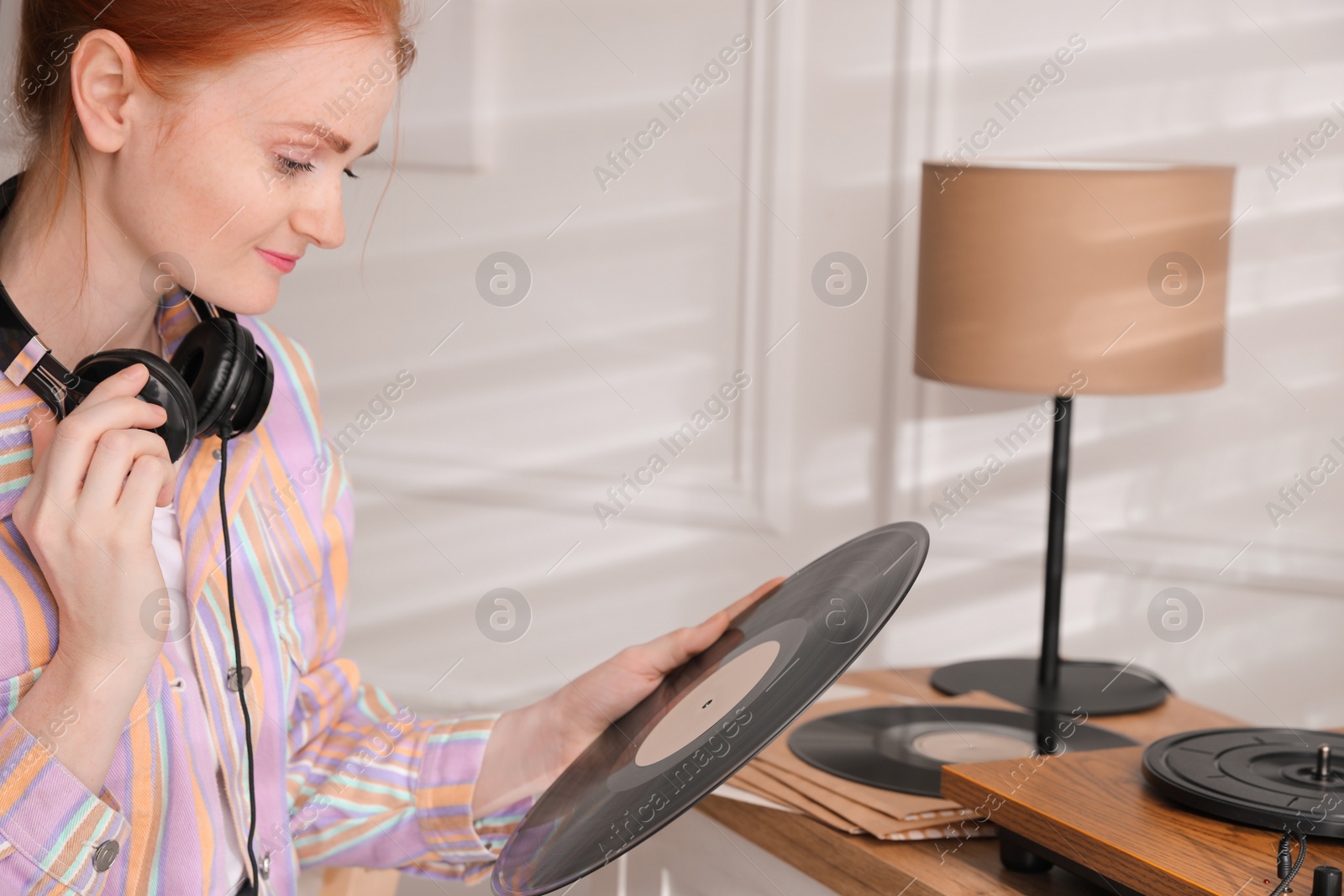 Photo of Young woman with vinyl disc near turntable at home