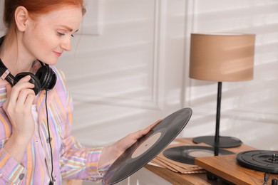 Young woman with vinyl disc near turntable at home