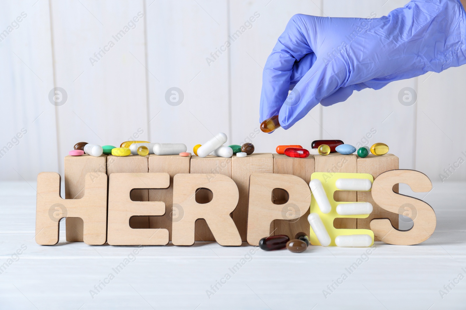 Photo of Woman in glove putting pill near word Herpes on white wooden table, closeup