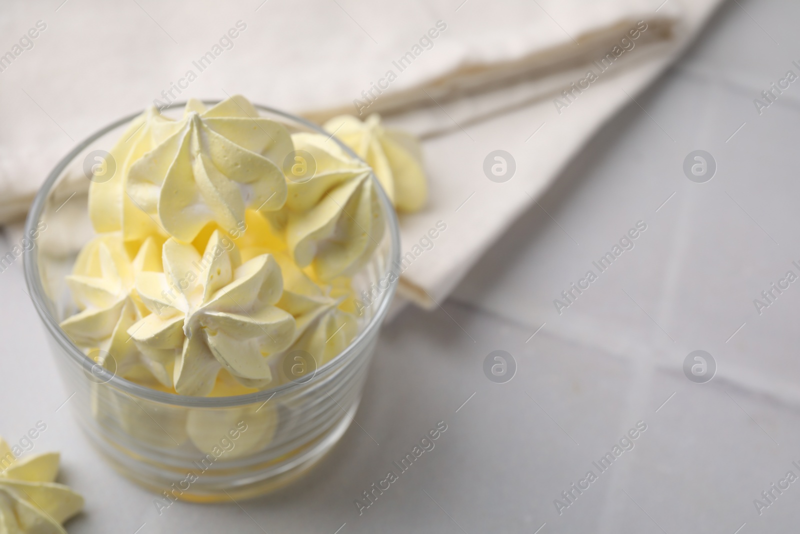 Photo of Tasty meringue cookies in glass on white tiled table. Space for text