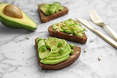 Photo of Crisp rye toast with sliced avocado on marble table