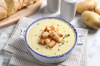 Photo of Tasty potato soup with croutons and rosemary in ceramic pot on white marble table