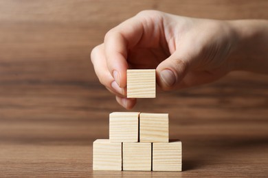 Photo of Woman building pyramid of cubes on wooden background, closeup with space for text. Idea concept