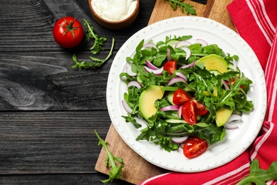 Photo of Delicious salad with avocado, arugula and tomatoes on black wooden table, flat lay