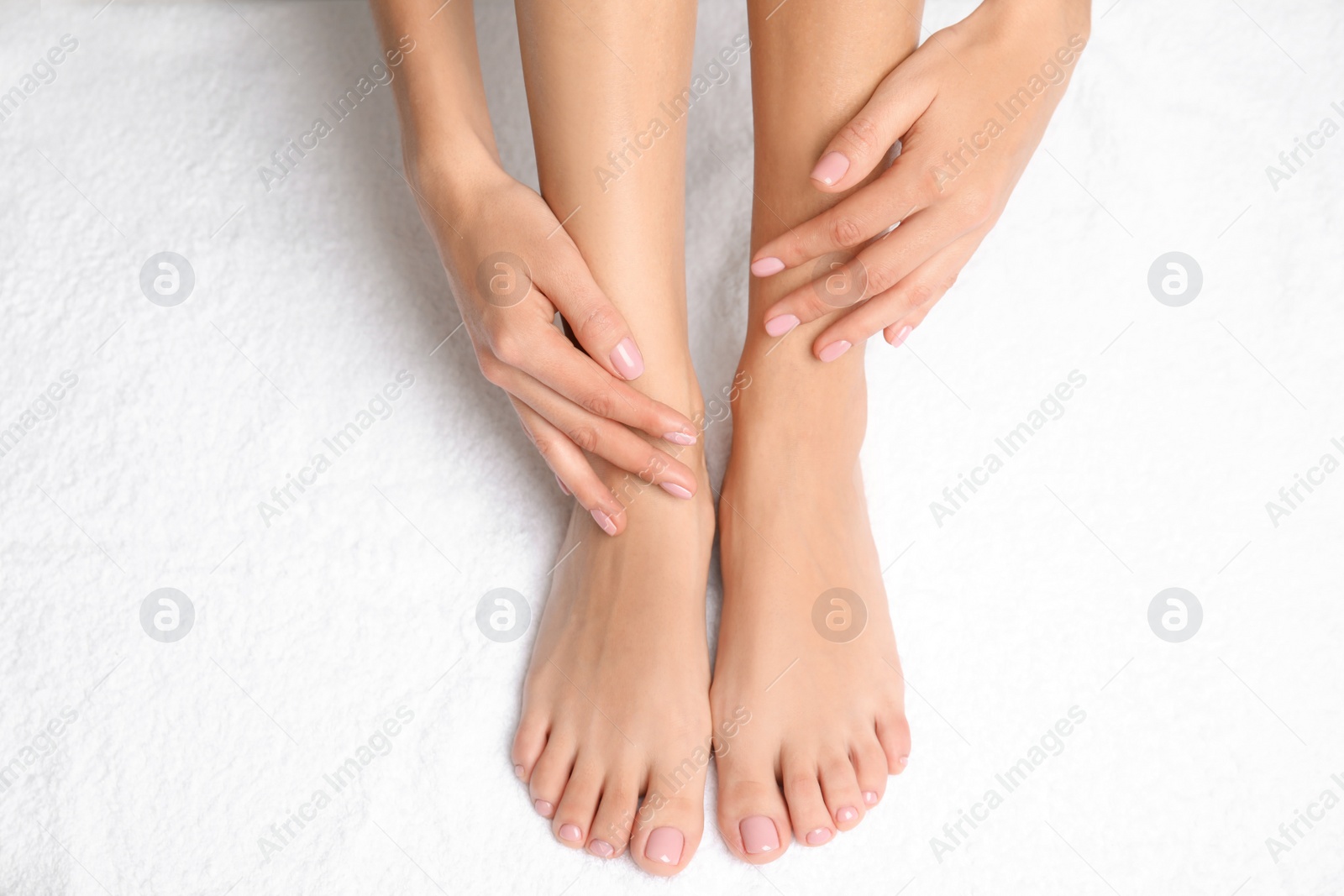 Photo of Woman touching her smooth feet on white towel, closeup. Spa treatment