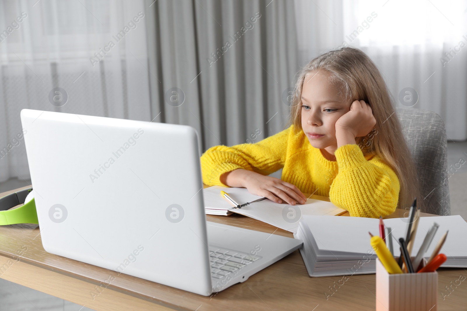 Photo of Cute little girl with modern laptop studying online at home. E-learning