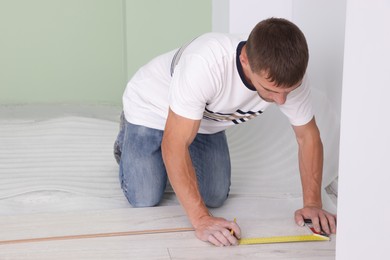 Photo of Man using measuring tape during installation of laminate flooring in room