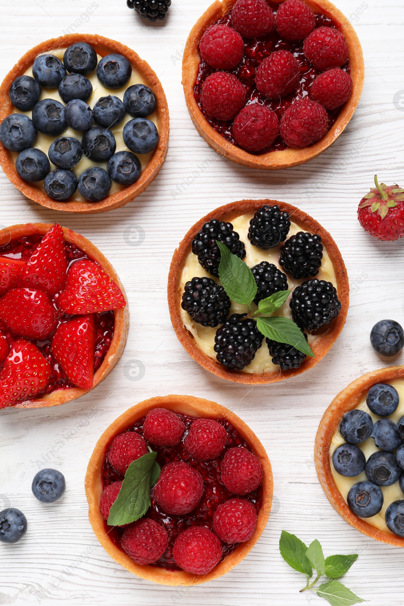 Photo of Tartlets with different fresh berries on white wooden table, flat lay. Delicious dessert