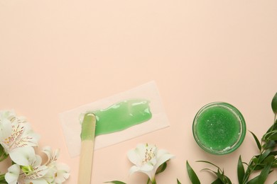 Wax with spatula, paper and flowers on beige background, flat lay. Space for text