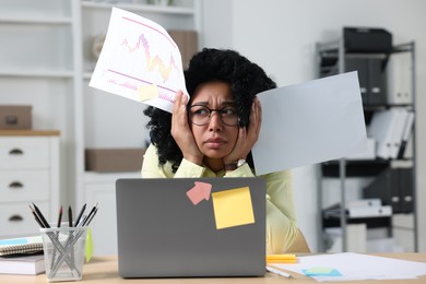 Deadline concept. Stressed woman with documents and charts near laptop in office