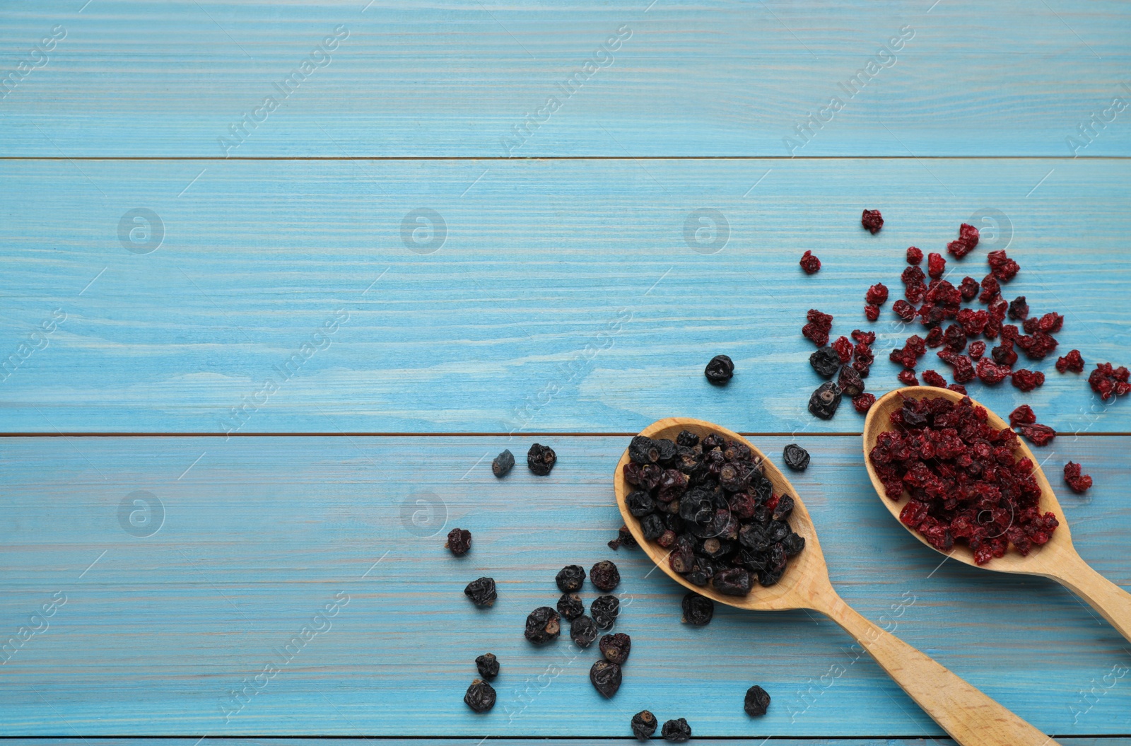 Photo of Dried red and black currant berries on light blue wooden table, flat lay. Space for text