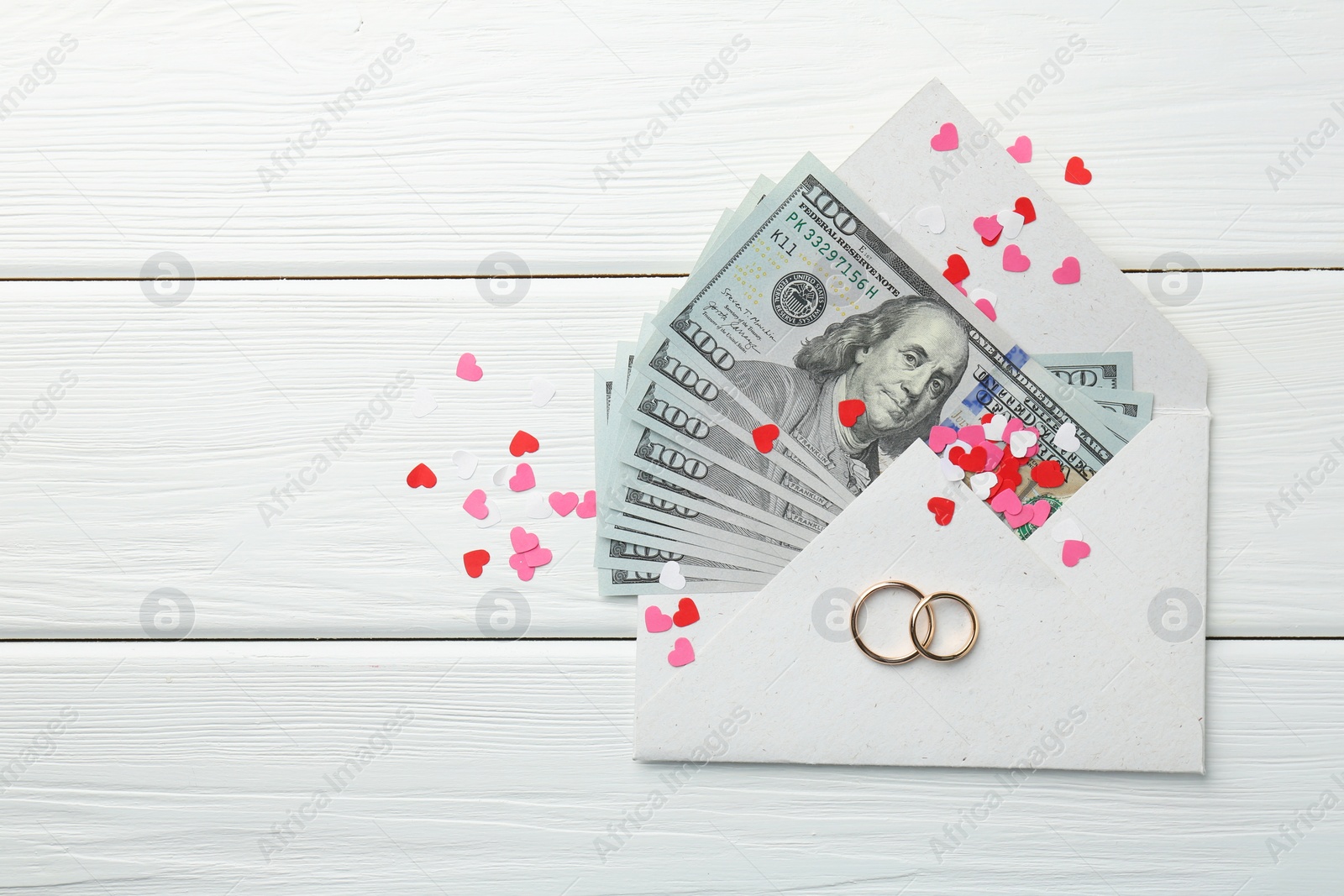 Photo of Honeymoon concept. Two golden rings, money and cutout hearts on white wooden table, flat lay. Space for text