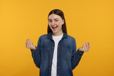 Happy woman showing money gesture on orange background