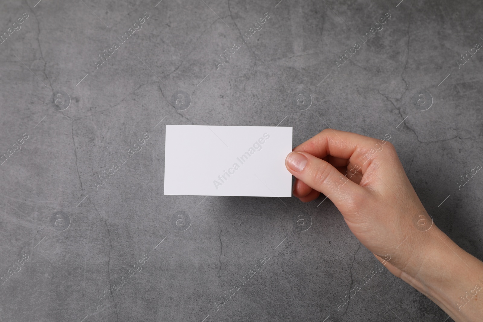 Photo of Woman holding blank card at grey table, top view. Mockup for design