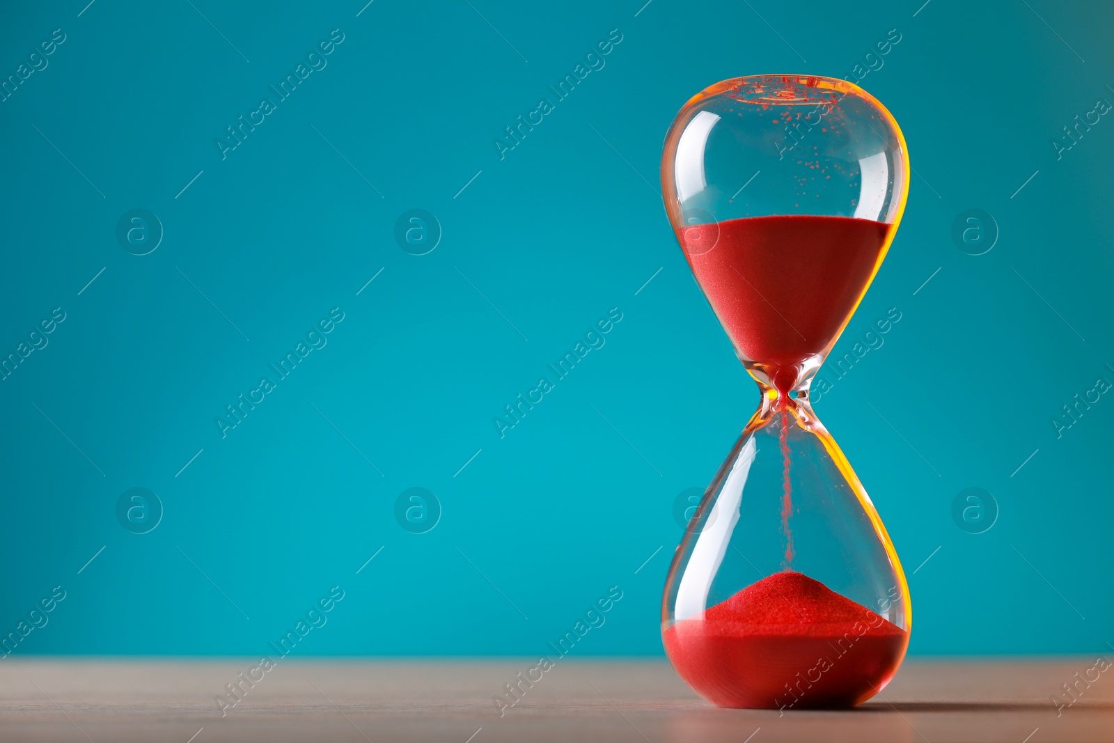 Photo of Hourglass with flowing red sand on table against light blue background, space for text