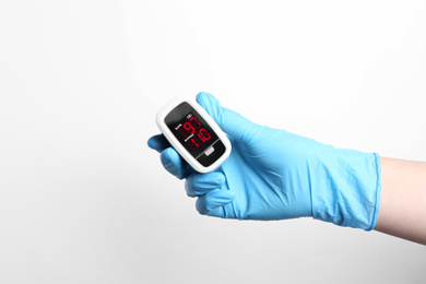Photo of Doctor in gloves holding fingertip pulse oximeter on white background, closeup
