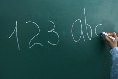 Photo of Little child writing letters and numbers on chalkboard, closeup
