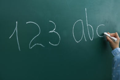 Little child writing letters and numbers on chalkboard, closeup