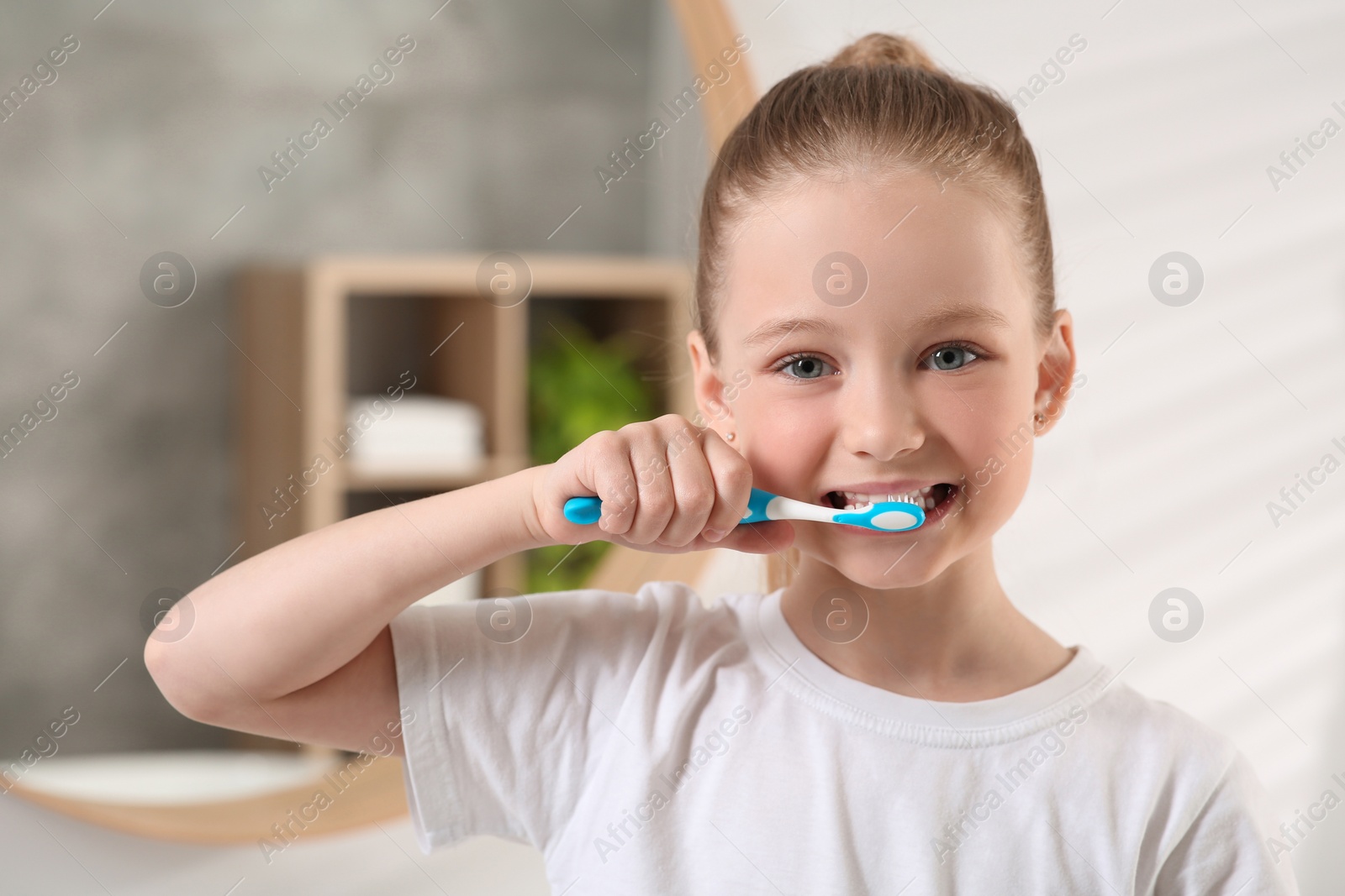 Photo of Cute little girl brushing her teeth with plastic toothbrush in bathroom