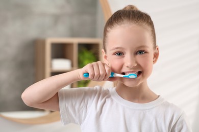 Cute little girl brushing her teeth with plastic toothbrush in bathroom