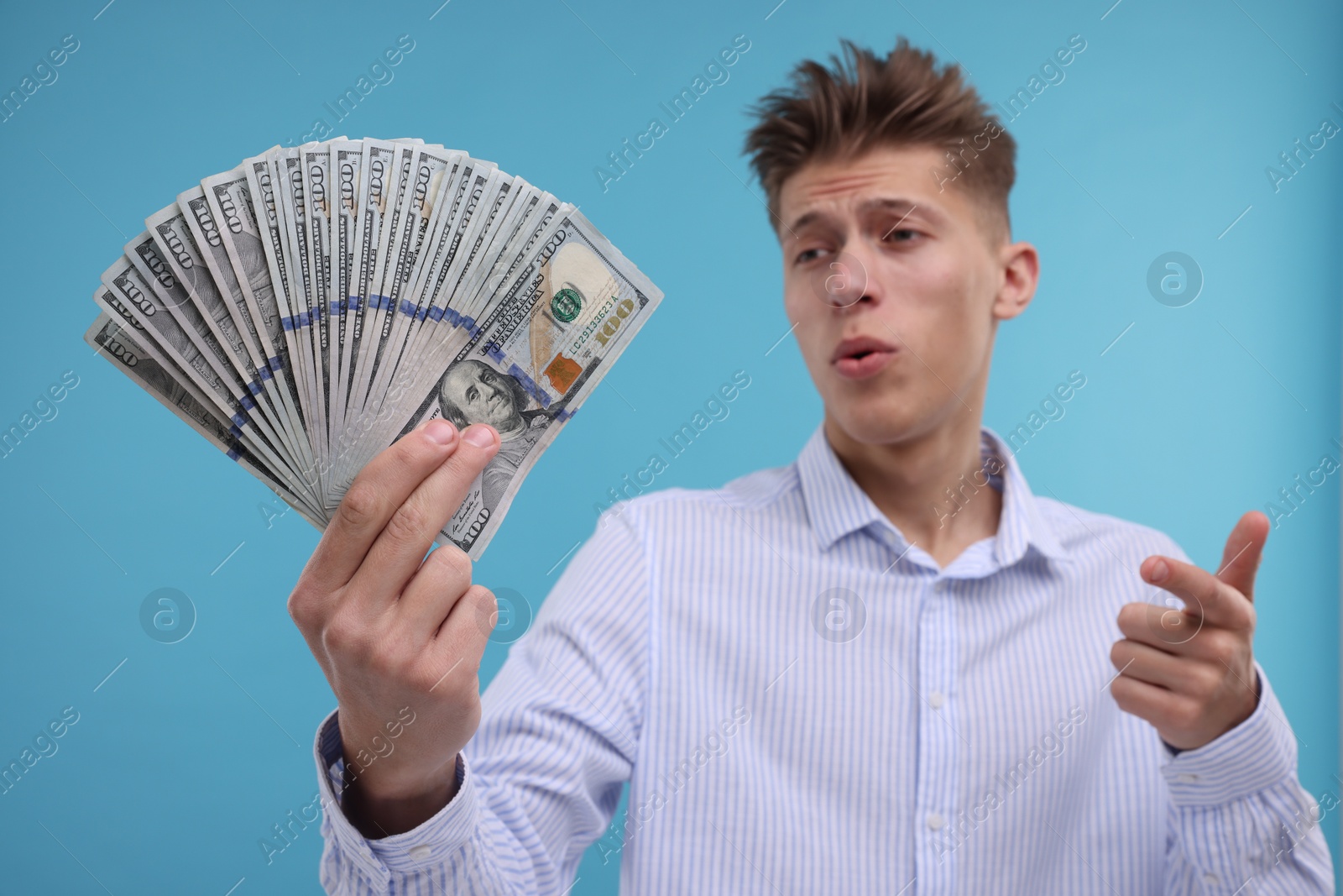 Photo of Handsome man pointing at dollar banknotes on light blue background, selective focus