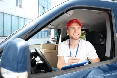 Photo of Young courier with clipboard and parcels in delivery car