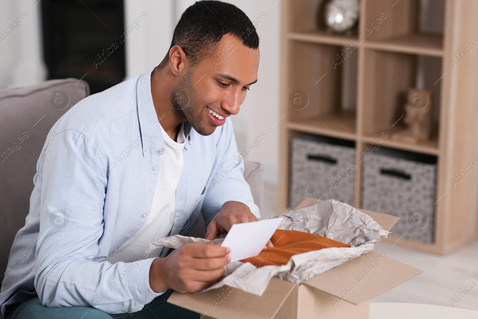 Photo of Happy man with greeting card near parcel at home. Internet shopping