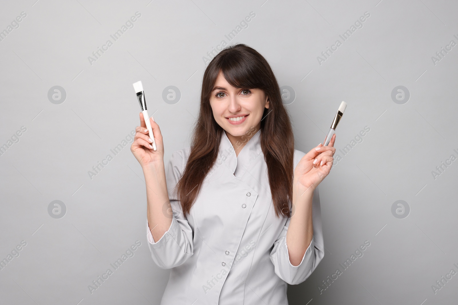 Photo of Cosmetologist with cosmetic brushes on grey background