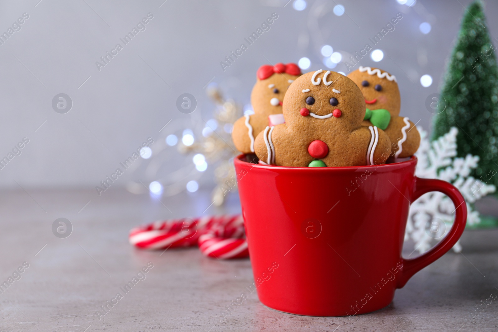 Photo of Gingerbread men in cup on light table against blurred lights, space for text