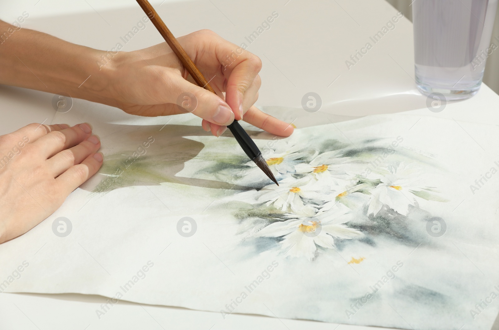 Photo of Woman painting flowers with watercolor at white table, closeup. Creative artwork