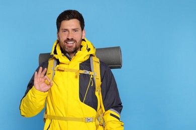 Photo of Happy man with backpack showing OK gesture on light blue background, space for text. Active tourism