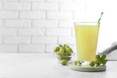 Photo of Tasty gooseberry juice in glass and fresh berries on light table. Space for text