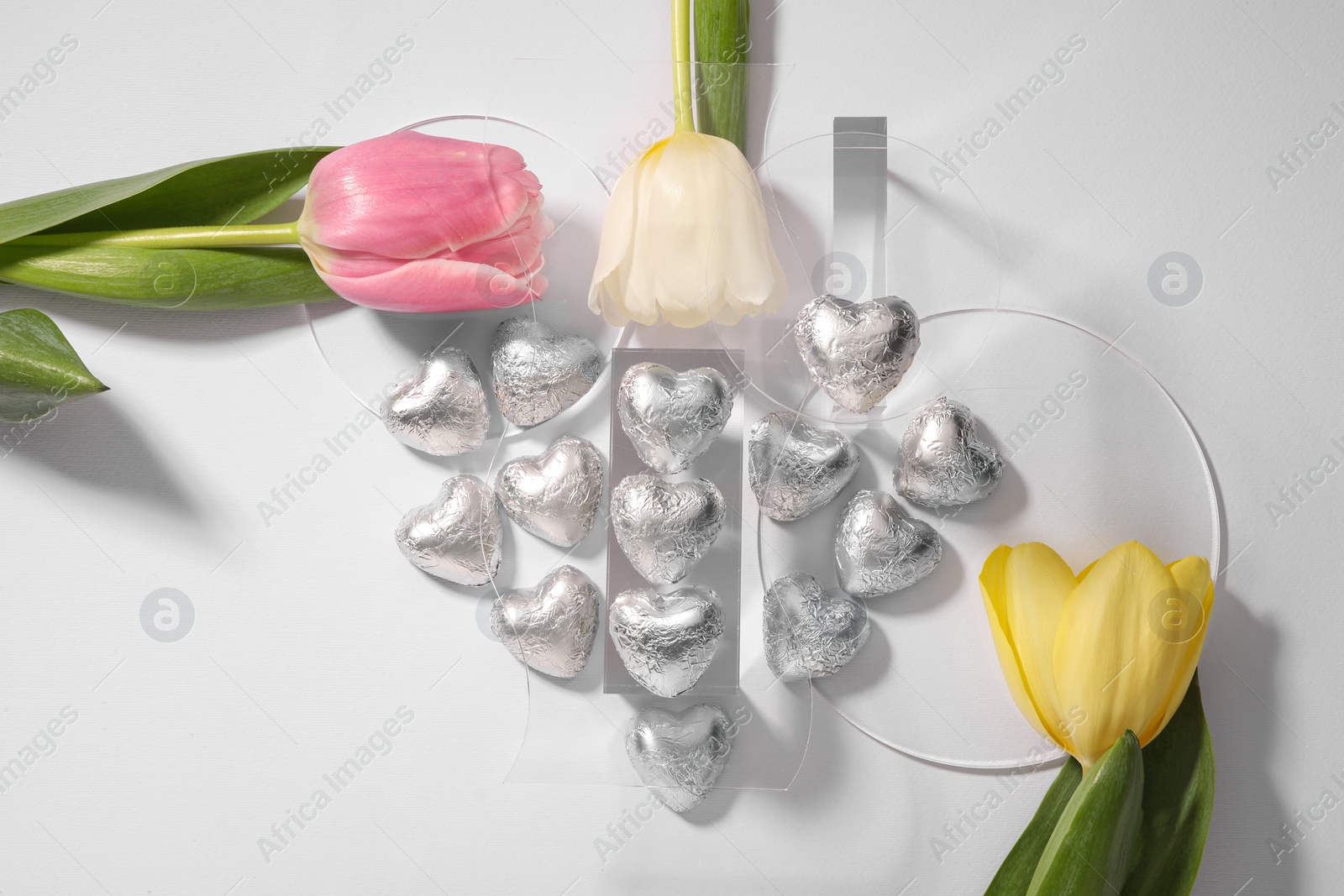 Photo of Heart made with delicious chocolate candies and beautiful tulips on white background, top view