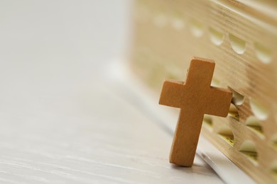 Christian cross near Bible on white wooden table, closeup. Space for text