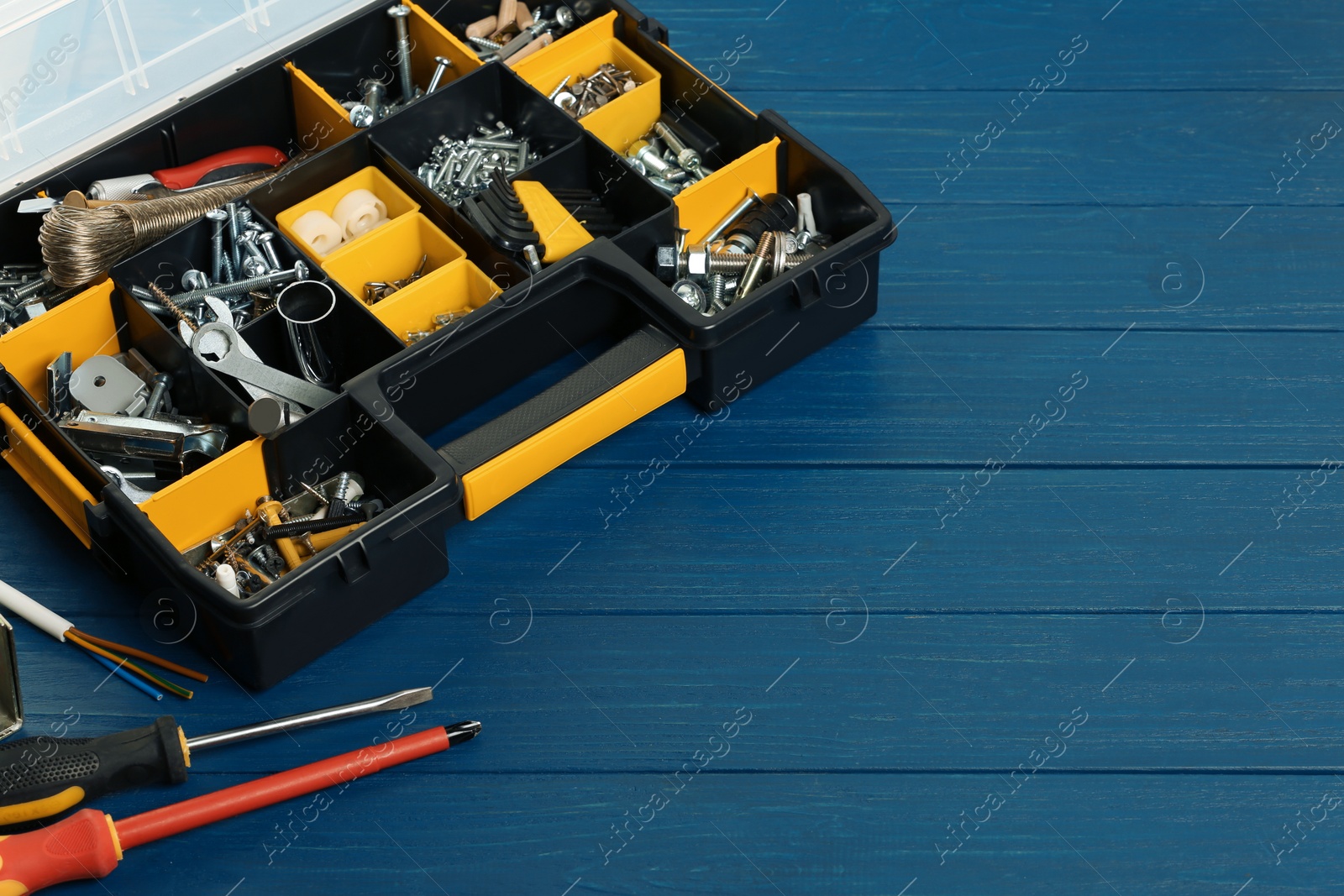 Photo of Plastic box with different furniture fittings and tools on blue wooden table, space for text