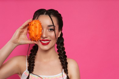 Photo of Young woman with fresh kiwano on pink background, space for text. Exotic fruit